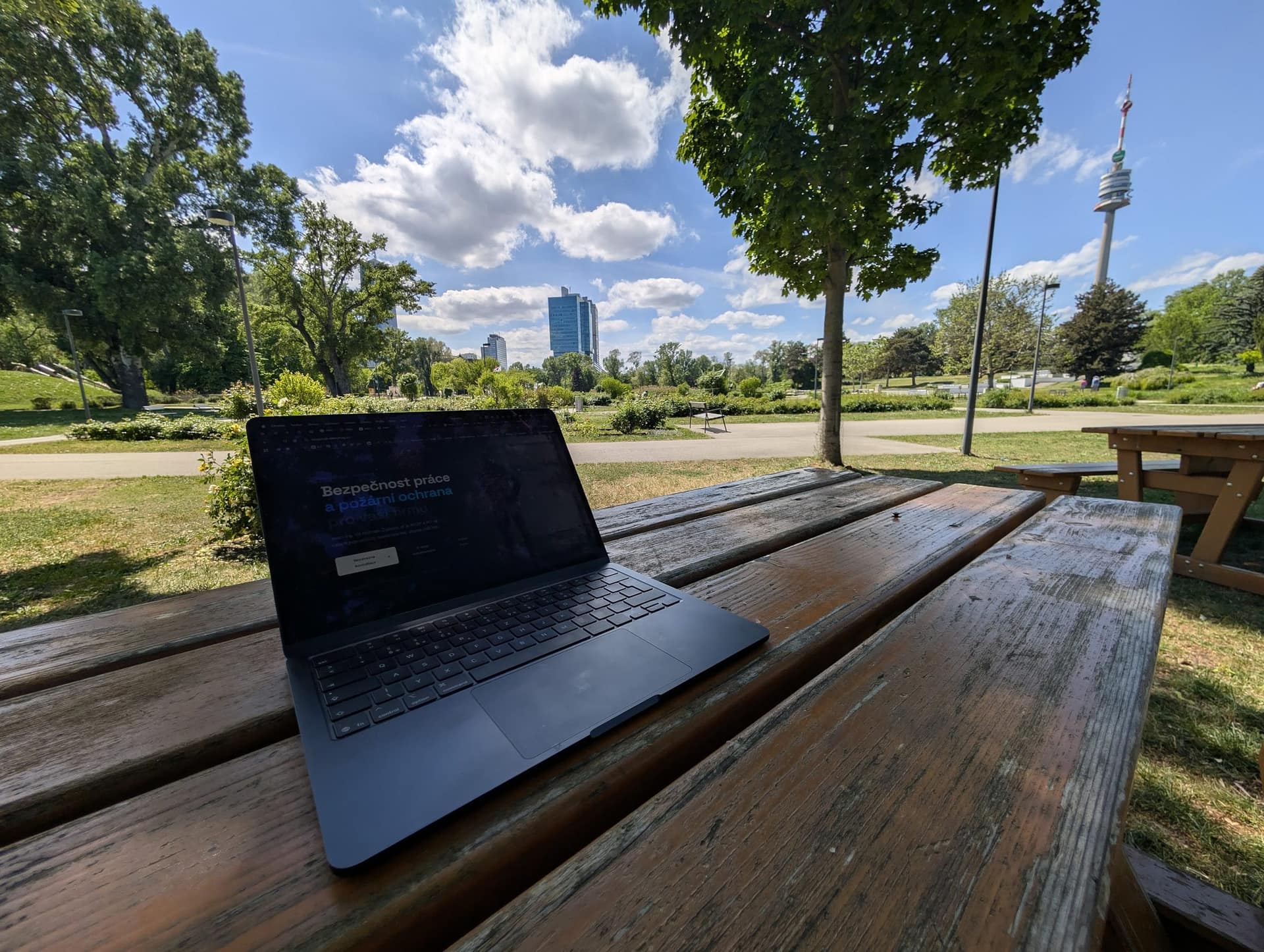 Notebook na lavičce v parku pod korunami stromů
